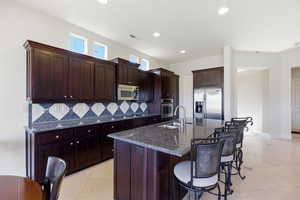 Kitchen with dark stone countertops, stainless steel appliances, a center island with sink, a kitchen bar, and light tile patterned flooring