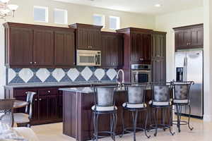 Kitchen featuring stainless steel appliances, an island with sink, light stone countertops, a kitchen bar, and tasteful backsplash