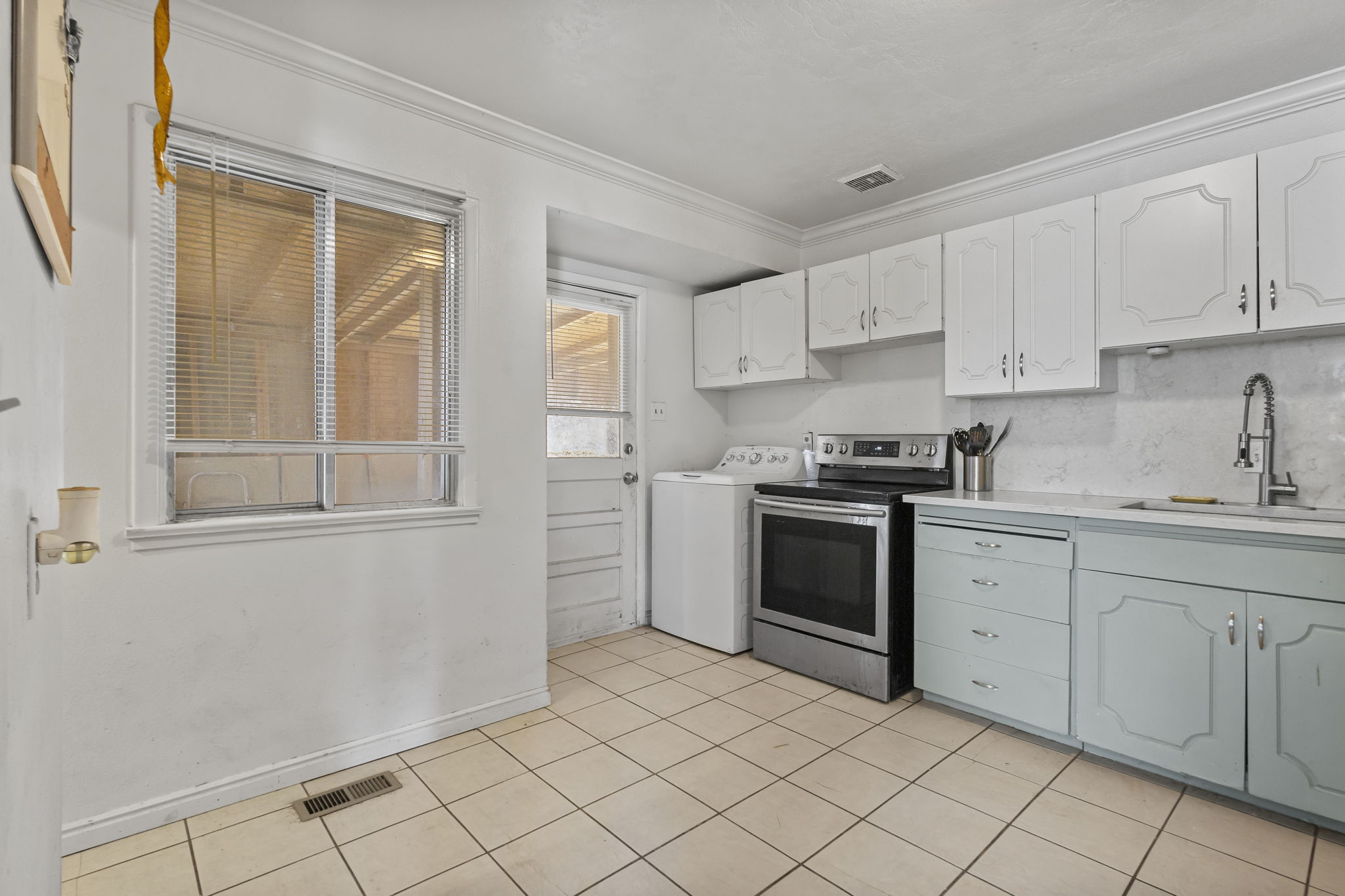 Dual tone kitchen with electric range, washer / dryer, ornamental molding, two tone cabinetry, and light tile patterned floors