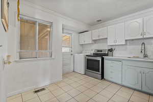 Dual tone kitchen with electric range, washer / dryer, ornamental molding, two tone cabinetry, and light tile patterned floors