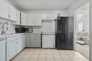 Kitchen featuring black appliances, ornamental molding, dual tone cabinetry, light countertops, and light tile patterned floors