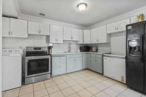 Dual tone kitchen featuring black appliances, washer / clothes dryer, light countertops, ornamental molding, and two tone cabinets