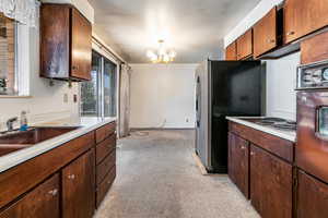 Kitchen featuring a chandelier, stainless steel appliances, light countertops, light colored carpet, and dark wood finish cabinets