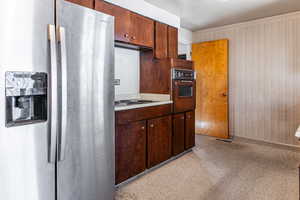 Kitchen with stainless steel fridge with ice dispenser, light countertops, light carpet, dark wood finish cabinetry, and electric stovetop