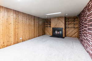 Unfurnished living room featuring carpet flooring, a glass covered fireplace, brick wall, and wooden walls