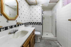 Full bathroom with wallpapered walls, a shower stall, vanity, and concrete floors