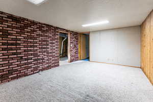 Finished below grade area with carpet floors, a textured ceiling, and brick wall
