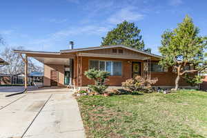 View of front facade with a front yard, brick siding, an attached carport, concrete driveway, and covered porch
