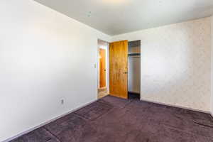 Unfurnished bedroom with wallpapered walls, carpet floors, and a closet