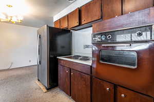 Kitchen featuring stainless steel fridge, light carpet, a chandelier, light countertops, and electric stovetop