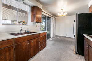 Kitchen featuring freestanding refrigerator, a chandelier, light countertops, and light colored carpet