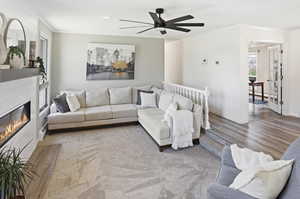 Living area with wood finished floors, crown molding, a large fireplace, ceiling fan, and baseboard heating