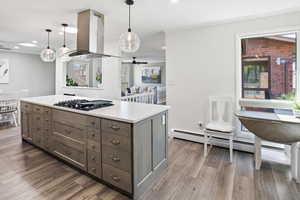 Kitchen with a center island, island range hood, light countertops, hanging light fixtures, and light wood finished floors