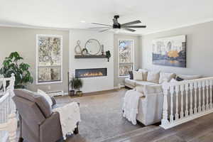 Living area featuring crown molding, a large fireplace, baseboard heating, ceiling fan, and wood finished floors