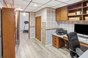 Office space with wallpapered walls, recessed lighting, light wood-type flooring, and a paneled ceiling