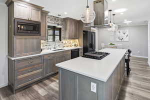 Kitchen with island exhaust hood, decorative backsplash, a center island, black appliances, and dark wood-style floors