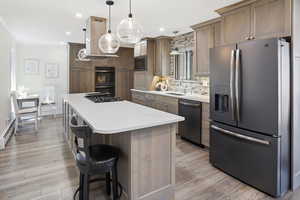 Kitchen with stainless steel appliances, island exhaust hood, light countertops, ornamental molding, and a kitchen bar