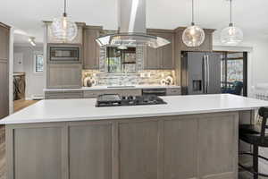 Kitchen featuring island range hood, a kitchen island, stainless steel appliances, tasteful backsplash, and a kitchen breakfast bar