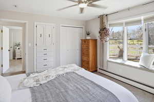 Bedroom with light carpet, a baseboard heating unit, ceiling fan, and a closet