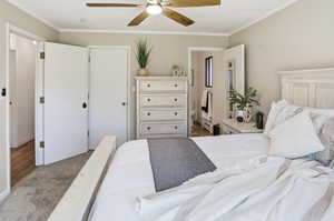 Bedroom with a closet, carpet, ornamental molding, a ceiling fan, and ensuite bathroom