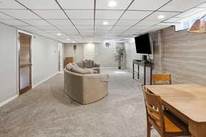 Living room with light colored carpet, a drop ceiling, recessed lighting, a baseboard radiator, and wood walls