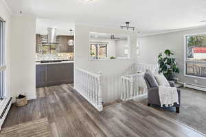 Sitting room featuring an upstairs landing, dark wood-style floors, baseboard heating, crown molding, and ceiling fan
