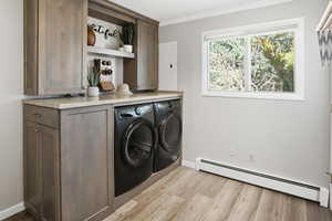Laundry room with a baseboard heating unit, separate washer and dryer, light wood-style flooring, crown molding, and electric panel