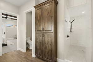Ensuite bathroom featuring a shower stall, light wood-style floors, a ceiling fan, and beam ceiling