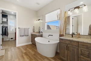 Bathroom featuring two vanities, light wood-style floors, a freestanding bath, recessed lighting, and a spacious closet