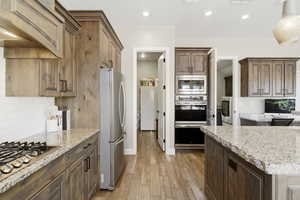 Kitchen featuring light stone countertops, stainless steel appliances, tasteful backsplash, light wood-style flooring, and recessed lighting