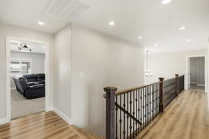 Corridor with light wood-type flooring, an upstairs landing, and a chandelier