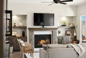 Living room featuring a glass covered fireplace, a ceiling fan, and wood finished floors