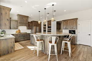Kitchen with a kitchen bar, pendant lighting, light stone countertops, light wood-style flooring, and stainless steel appliances