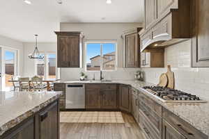 Kitchen featuring light stone countertops, stainless steel appliances, tasteful backsplash, light wood finished floors, and dark wood finish cabinetry