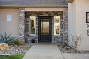 Property entrance with stone siding, stucco siding, and covered porch