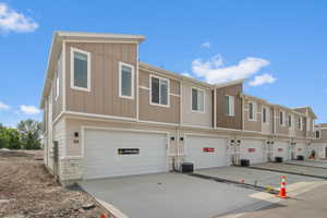 View of front of property featuring stone siding, an attached garage, board and batten siding, driveway, and a residential view