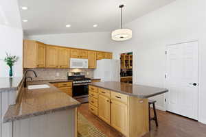 Kitchen with white appliances, vaulted ceiling, a kitchen breakfast bar, pendant lighting, and decorative backsplash