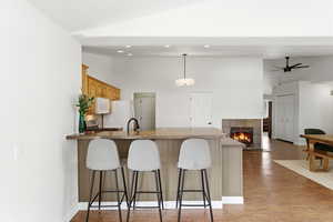 Kitchen with a kitchen breakfast bar, a tile fireplace, light wood-type flooring, a peninsula, and vaulted ceiling
