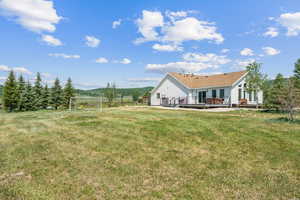 Back of house featuring a wooden deck, a lawn, and a rural view