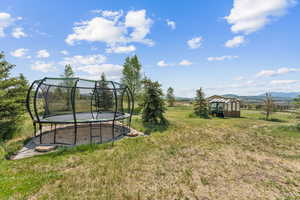 View of green lawn with a trampoline, a mountain view, and an outdoor structure