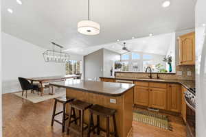 Kitchen with a center island, vaulted ceiling, dark wood-style flooring, stainless steel range with gas cooktop, and tasteful backsplash