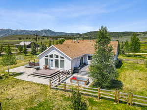 Rear view of property with stucco siding, a deck with mountain view, a view of countryside, a fenced backyard, and a gate