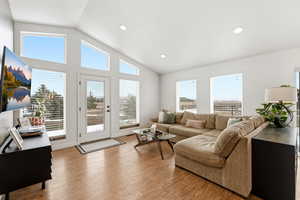 Living area with vaulted ceiling, wood finished floors, healthy amount of natural light, and recessed lighting