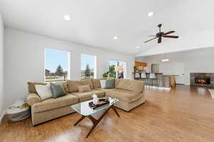 Living area featuring ceiling fan, light wood-type flooring, a tiled fireplace, recessed lighting, and vaulted ceiling