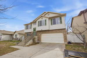 Raised ranch featuring brick siding, driveway, and an attached garage