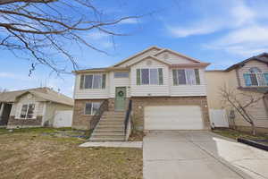 Raised ranch with brick siding, concrete driveway, a garage, and a front lawn