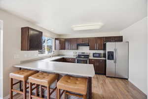 Kitchen featuring a breakfast bar area, dark wood finish cabinets, a peninsula, and stainless steel appliances