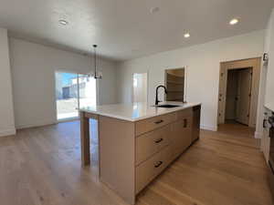 Kitchen featuring a kitchen island with sink, light wood-type flooring, a chandelier, light stone countertops, and light wood finish cabinets