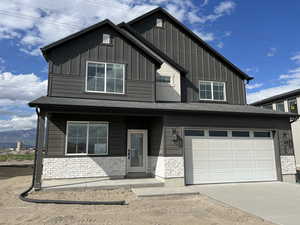 View of front of house with board and batten siding, stone siding, concrete driveway, covered porch, and a garage