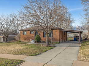 View of front of home with an attached carport, brick siding, a front yard, and concrete driveway